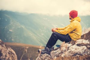 excursionista sentado en una roca divisando la vista desde una montaña