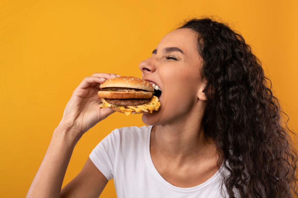 mujer comiendo hamburguesa con fondo naranja